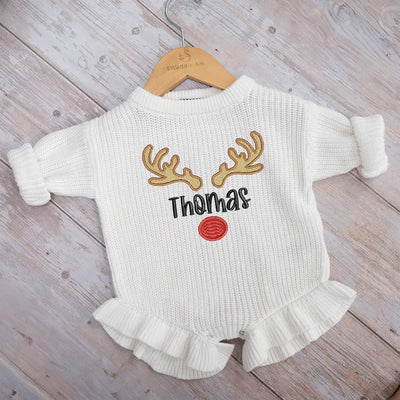 White baby romper with reindeer design and 'Thomas' text on a wooden surface