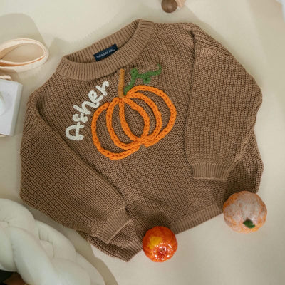 Brown sweater with a pumpkin design and 'Asher' text on a light background