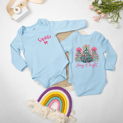 Two light blue baby onesies with Christmas designs on a white surface with decorative items.