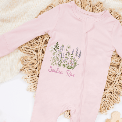 Pink baby onesie with floral design and 'Sophia Rae' text on a textured surface