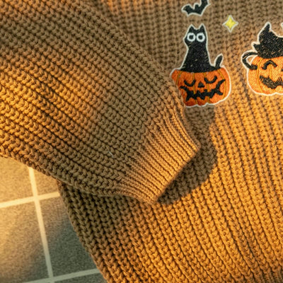 Brown knitted sweater with Halloween-themed patches on a tiled floor.