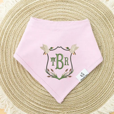 Pink baby bib with embroidered initials 'TBR' on a woven mat