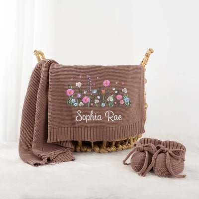 Brown knitted blanket with floral embroidery and baby booties on a white background