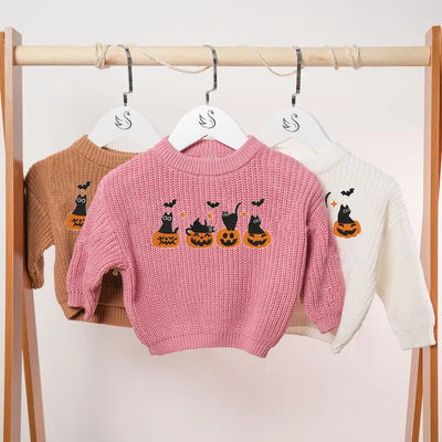 Pink sweater with Halloween design on a rack with other sweaters.