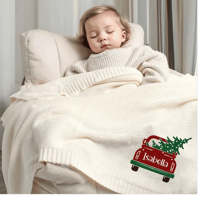 Child wrapped in a cream custom blanket with a personalized Christmas tree in the car design, lying on a bed.