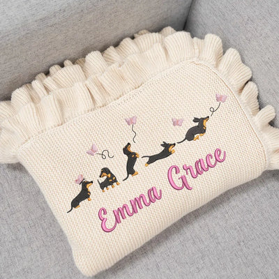 Cream personalized baby blanket with embroidered dachshunds and 'Emma Grace' text on a gray surface