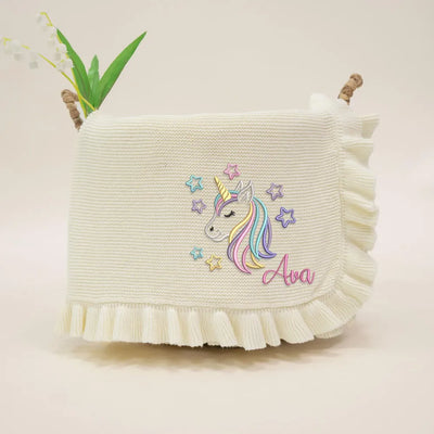 Cream personalized baby blanket with embroidered unicorn design and name 'Ava' on a light background