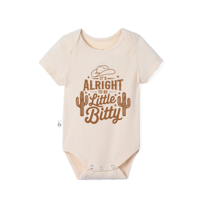 A short-sleeve baby bodysuit in a light cream color with a brown western-themed graphic that reads 'It's Alright to be Little Bitty' with a cowboy hat and cactus design, shown on a plain white background.