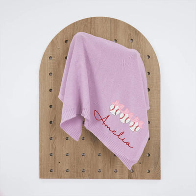 Lilac personalized baby blanket with embroidered name and baseball bow design on a wooden surface