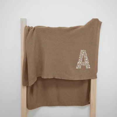 Mocha personalized baby blanket with a floral letter 'A' on a wooden rack against a white background