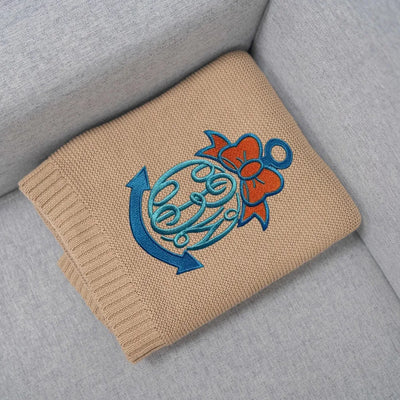 Personalized baby blanket with blue and orange anchor design on a gray surface