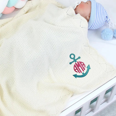 Baby wrapped in a personalized blanket with an embroidered anchor and initials, lying in a crib.