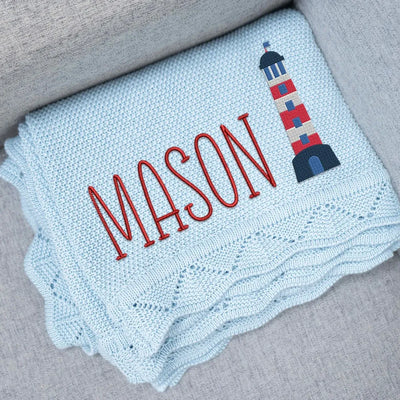 Personalized baby blanket with embroidered name 'Mason' and a lighthouse design on a gray surface.