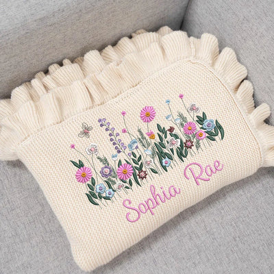 Cream personalized baby blanket with wildflower embroidery and 'Sophia Rae' text on a gray surface