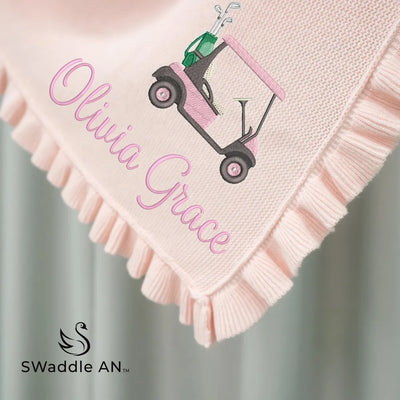 Pink personalized baby blanket with golf cart design and 'Olivia Grace' text, featuring the brand 'SWaddle AN'.