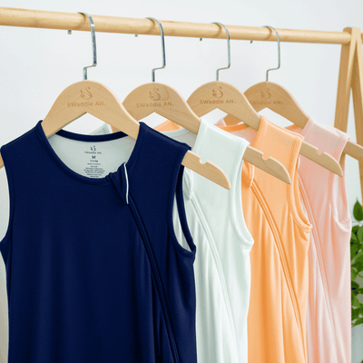 Four sleeveless tops in blue, white, orange, and pink hanging on wooden hangers against a light background.